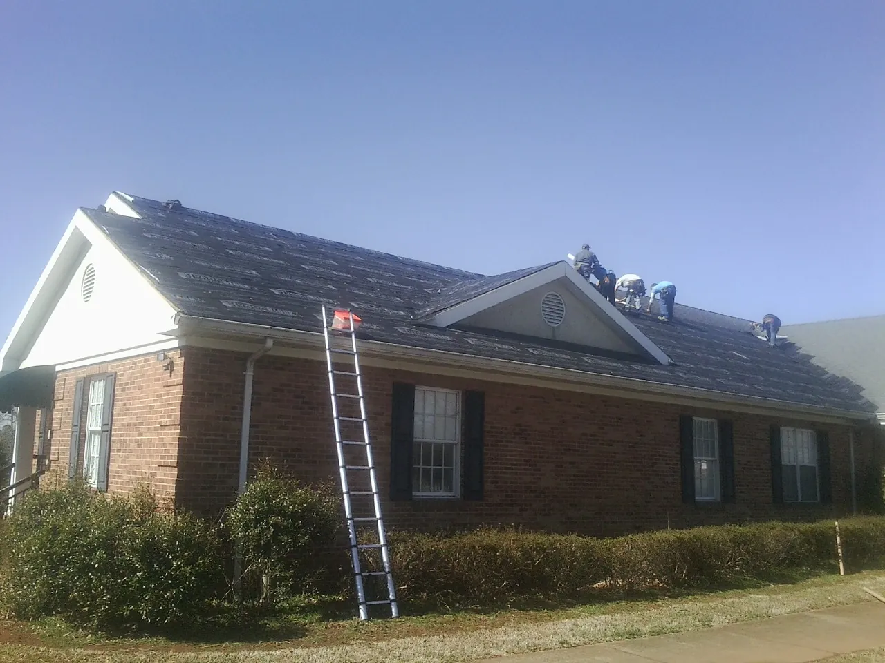 Crew tearing shingles off a brick ranch roof with a ladder set — Emergency Roof Repair work by our crew in Hamilton