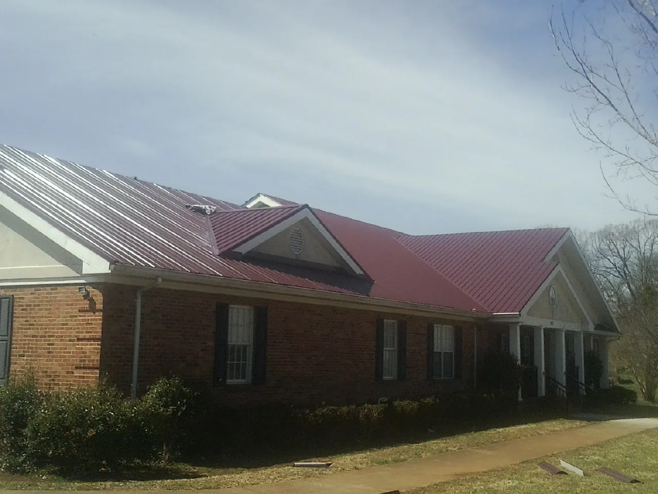 Red metal roof with gabled entries on a long brick building, from a Hail Damage Roof Repair job in Hamilton